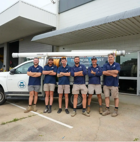 Members from Tropical Coast Plumbing stand smiling in front of a branded work vehicle parked outside their office.