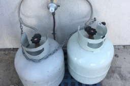 Close-up of two LPG gas bottles connected with a regulator and piping, part of a residential gas fitting service in Yeppoon.