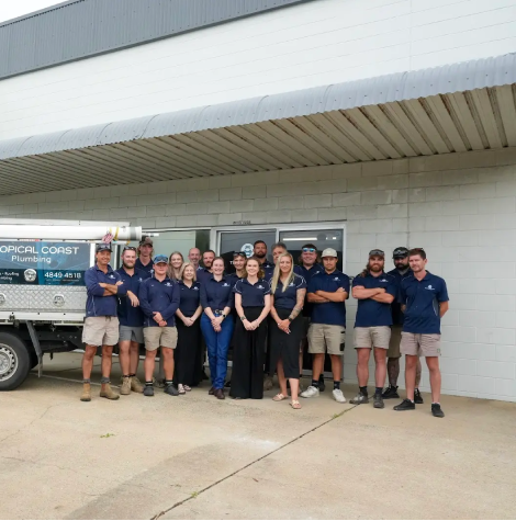 Members from Tropical Coast Plumbing stand smiling in front of a branded work vehicle parked outside their office.
