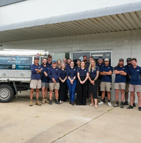 Members from Tropical Coast Plumbing stand smiling in front of a branded work vehicle parked outside their office.