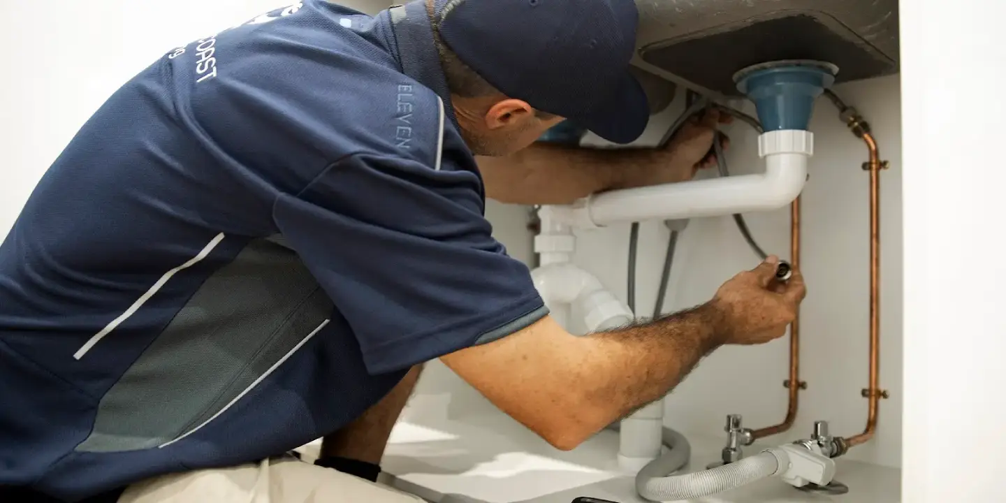 Townsville plumber repairing a blocked drain pipe under a kitchen sink with professional plumbing tools.