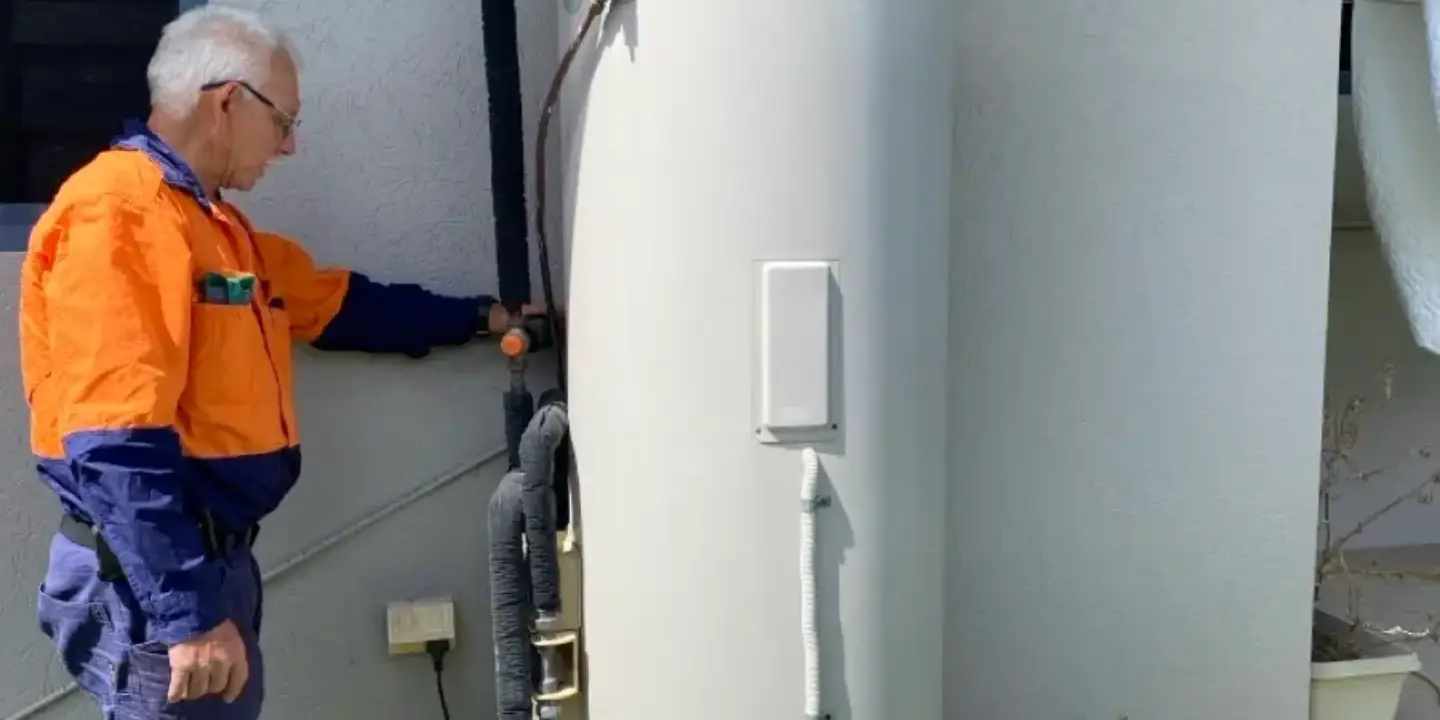 Licensed plumber in Townsville repairing a hot water system unit and checking pipes to ensure a reliable hot water supply.