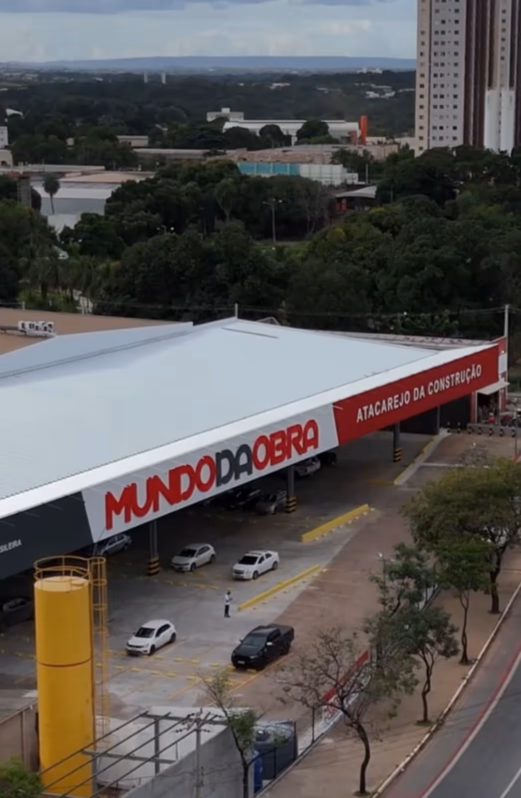 Aerial view of Mundo da Obra construction supply store with parked cars and surrounding trees.