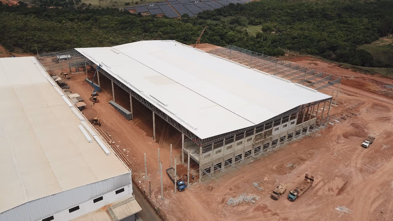 Aerial view of a large industrial warehouse under construction with white roofing and surrounding dirt area with construction vehicles.