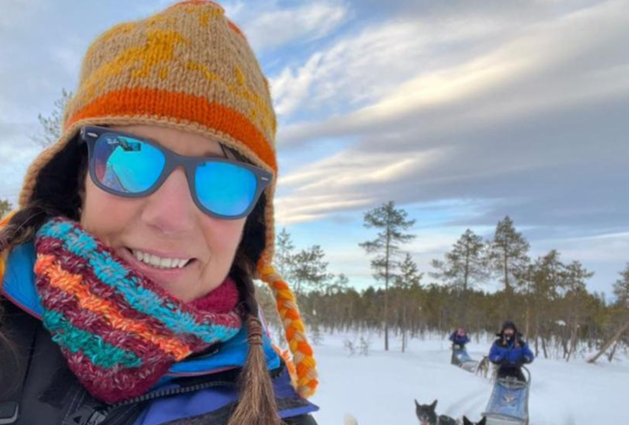 Lapland. She is wearing a bright blue warm ski jacket and a yellow and orange knitted hat.