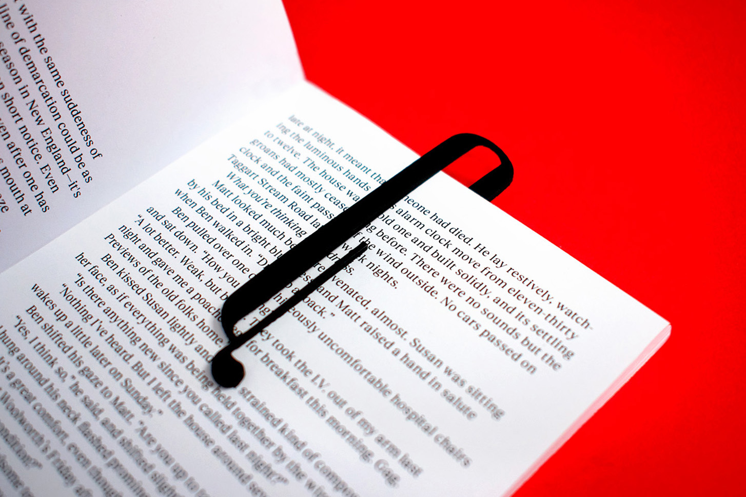 Close up photograph of an open book with a custom bookmark in the shape of the logo placed on top.
