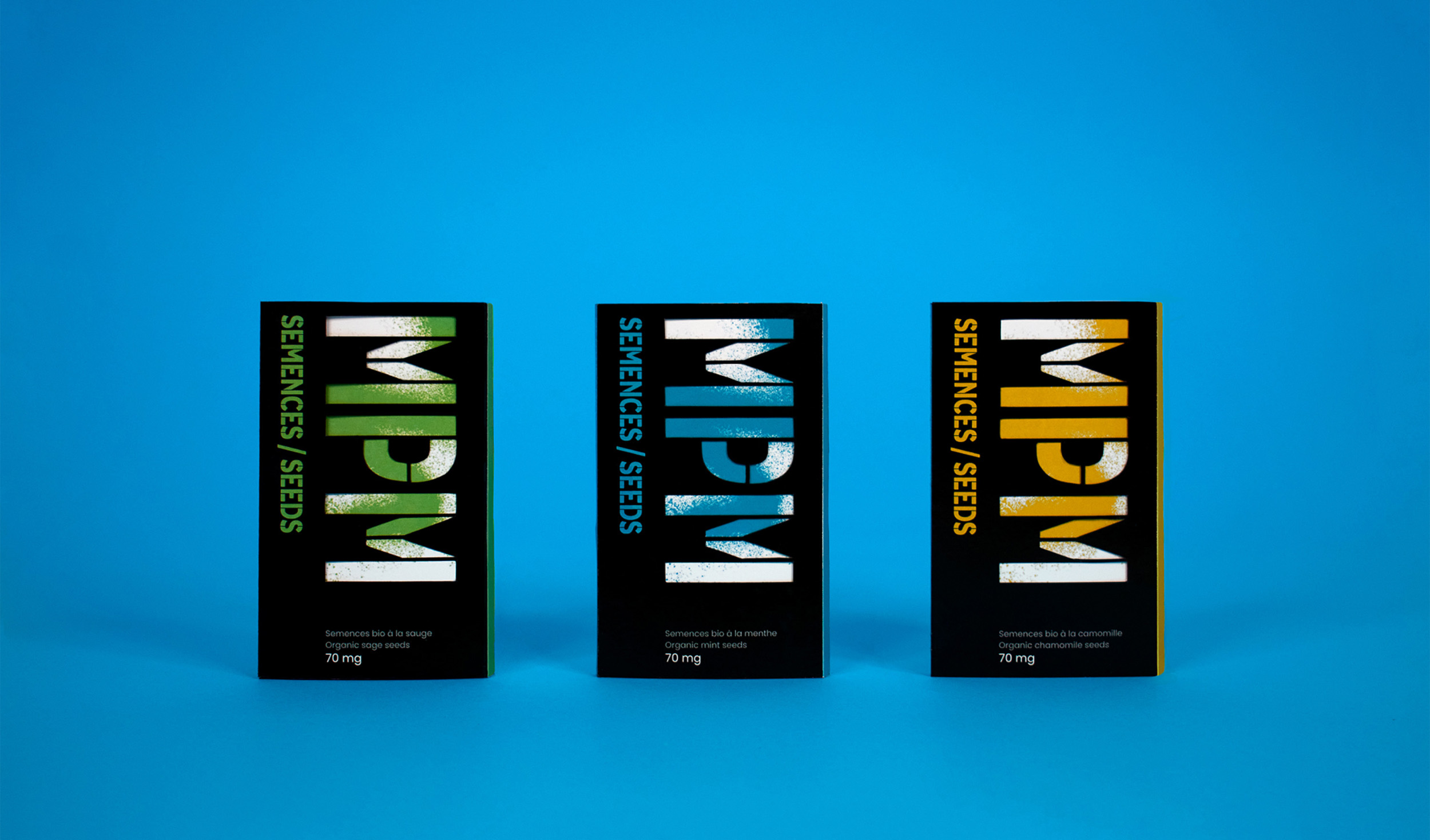 3 package facings (all representing different seeds: On the left, sage, which is represented by a green shade. In the middle, mint, which is associated to a bright blue. On the right, chamomile, which is associated to an orange-yellow shade. All packagings are standing vertically and directly facing the camera and separated by around an inch. The packages are placed on a bright blue background (the same blue associated to the mint seeds).