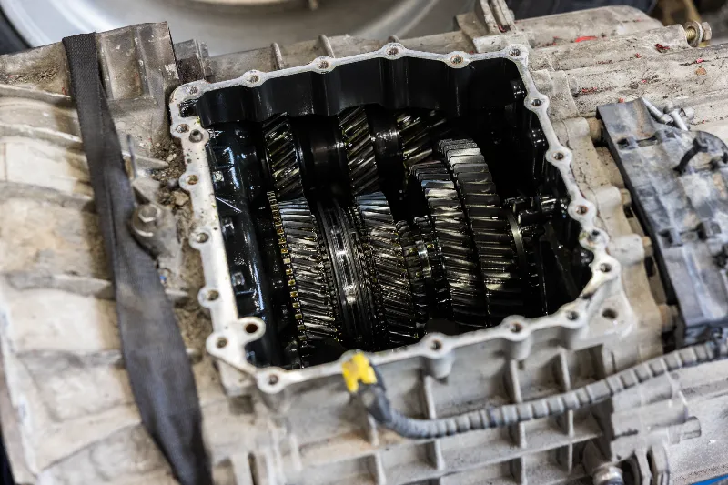Transmission repair showing exposed gear train coated in oil inside an opened heavy-duty gearbox housing.