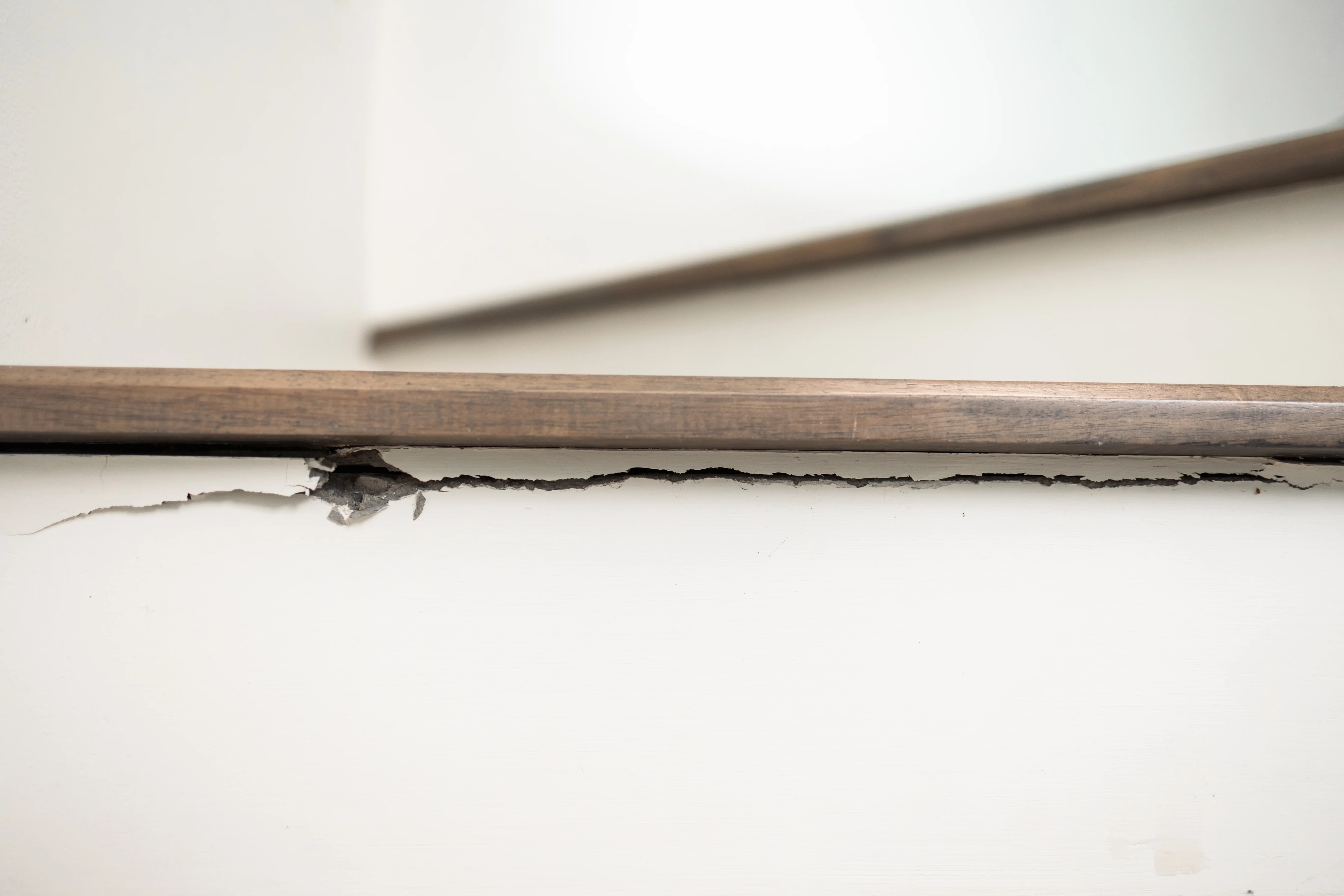 Close-up of a chipped and cracked wooden stair edge with peeling white paint underneath.