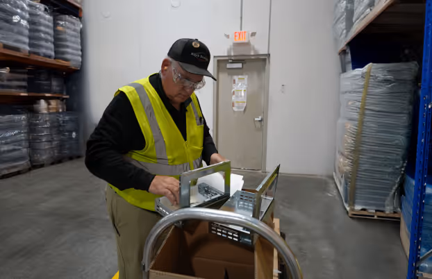 Worker in a yellow safety vest and black cap assembling metal traps inside a warehouse.