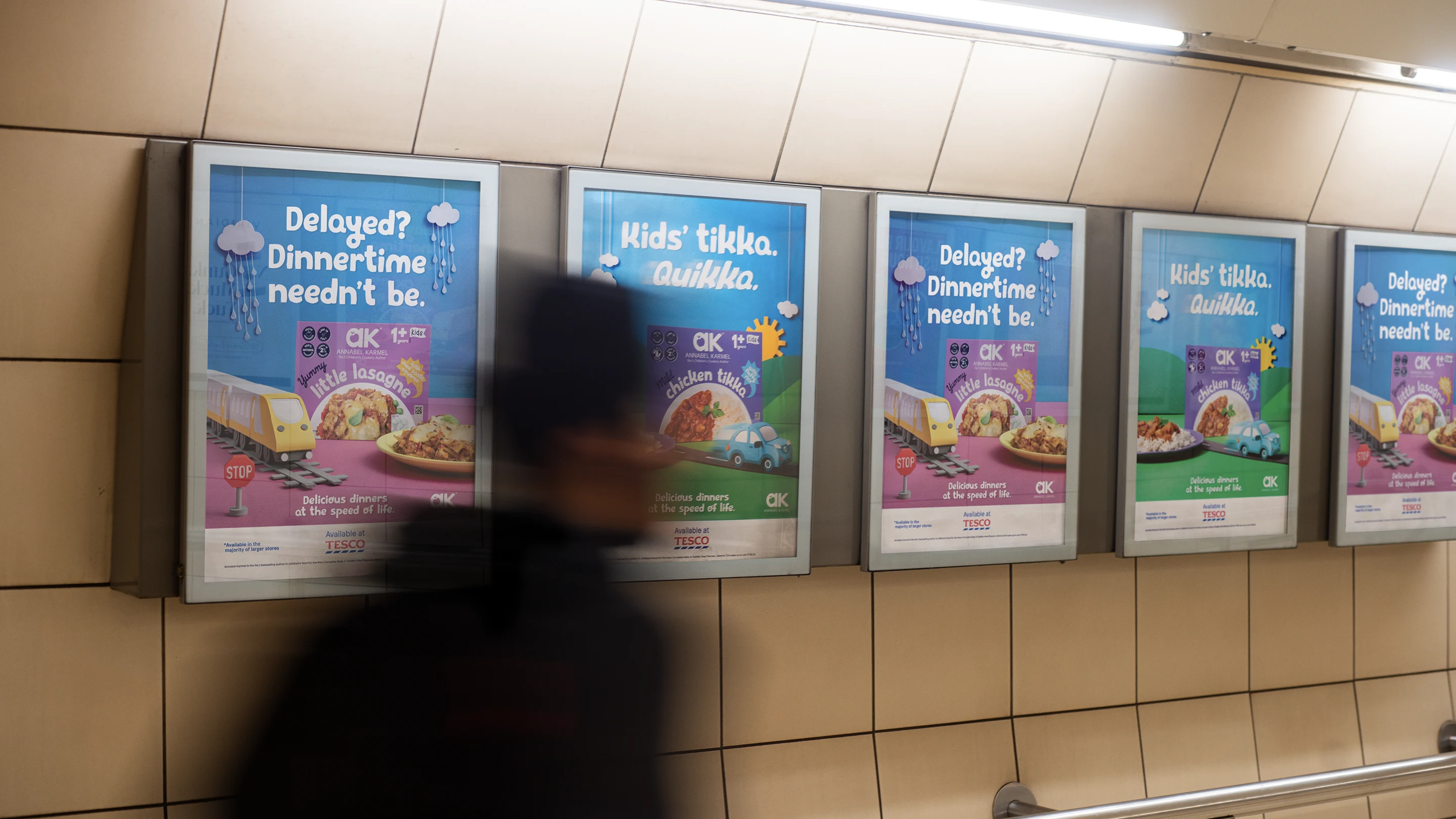 Blurred person walking past four framed advertisements in a tiled subway corridor, promoting Annabel Karmel kids' meals with phrases like 'Delayed? Dinnertime needn’t be' and 'Kids’ tikka. Quikka.'