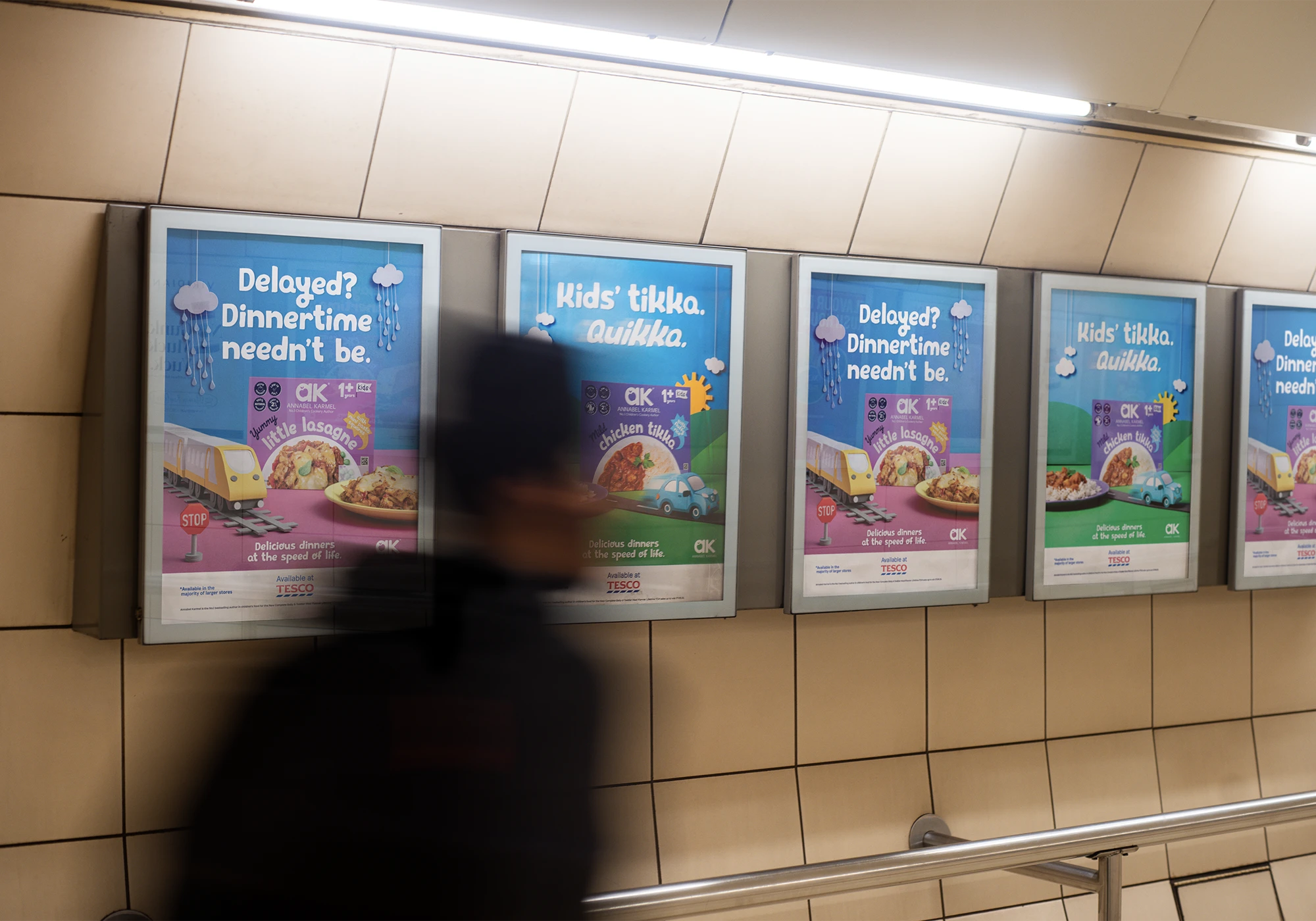 Blurred person walking past four framed advertisements in a tiled subway corridor, promoting Annabel Karmel kids' meals with phrases like 'Delayed? Dinnertime needn’t be' and 'Kids’ tikka. Quikka.'