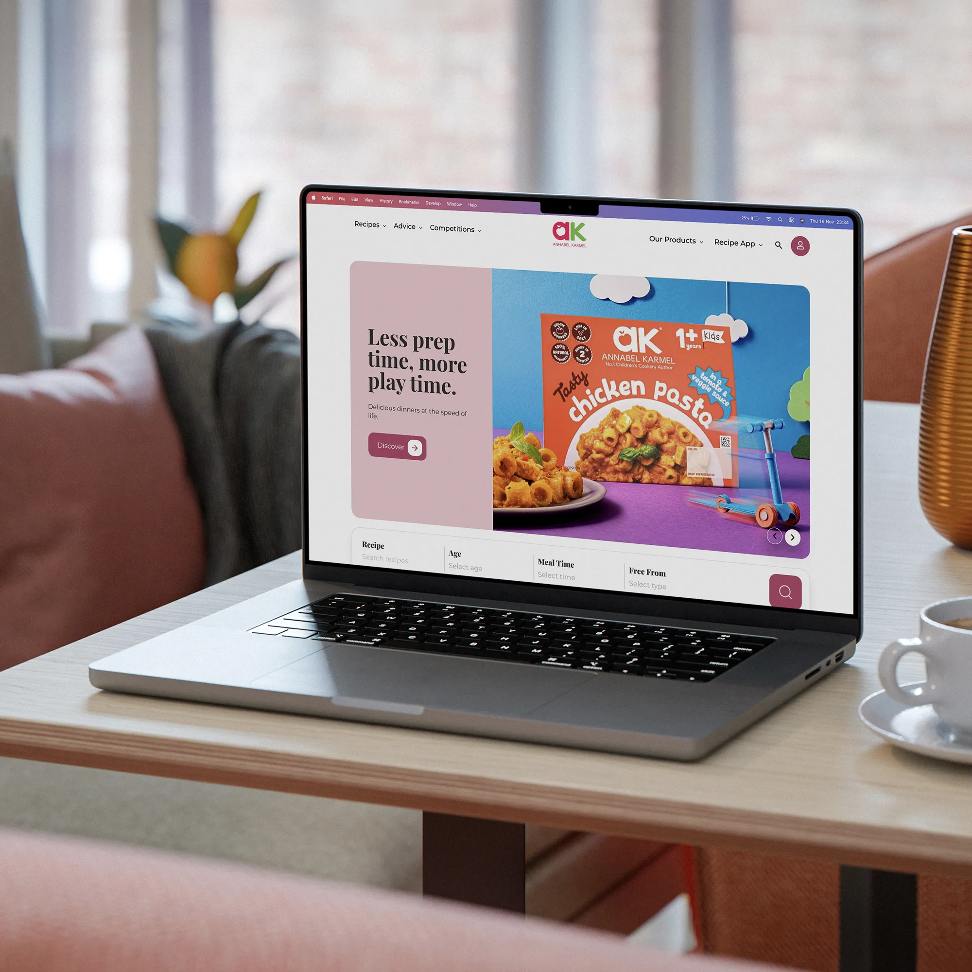 Open laptop on a table displaying a colorful webpage about Annabel Karmel's tasty chicken pasta with a slogan 'Less prep time, more play time.'