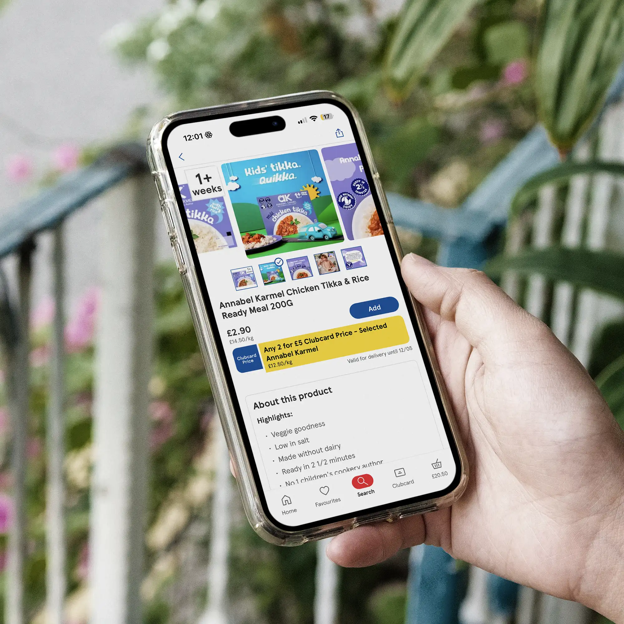 Hand holding smartphone displaying an online product page for Annabel Karmel Chicken Tikka & Rice Ready Meal with price and product details.