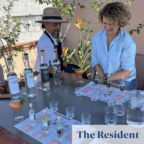Hombre y mujer disfrutando una degustación de mezcal al aire libre con varias botellas y copas sobre la mesa.