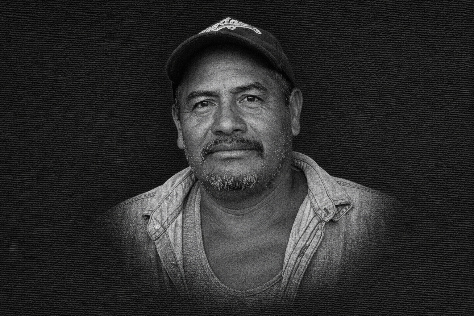 Retrato en blanco y negro de un hombre afroamericano con gorra y camisa de mezclilla, mirando al frente con expresión serena.