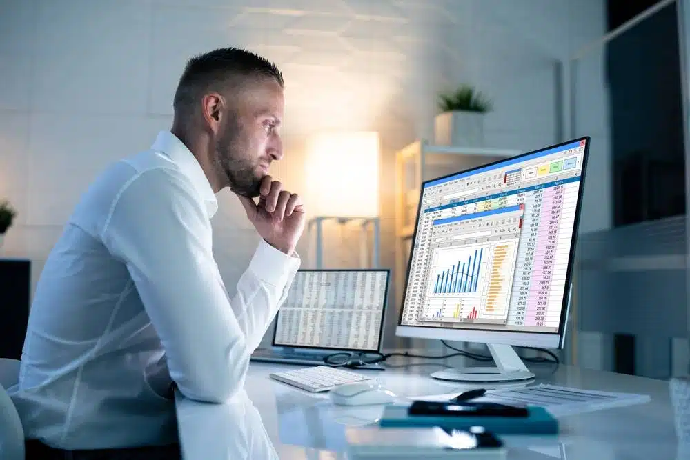 Professionnel de la finance analysant un tableau de chiffres sur deux écrans