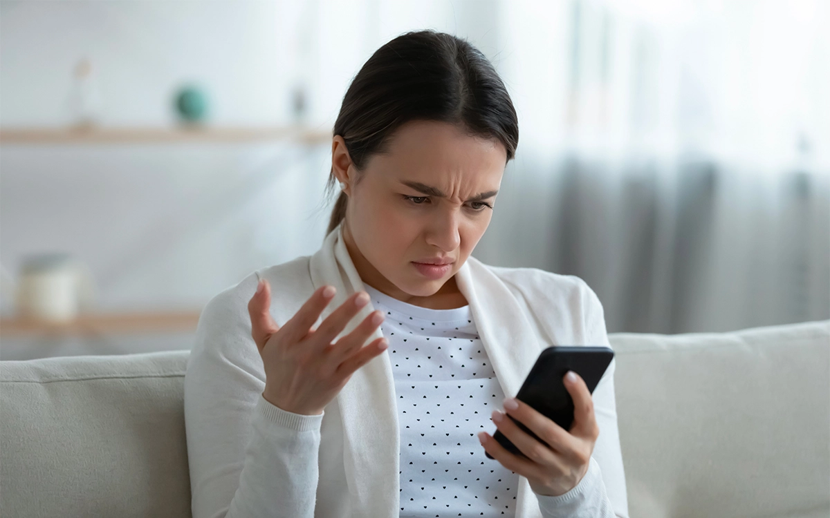 Femme agacée regardant son smartphone lent, assise sur un canapé