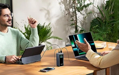 Homme travaillant sur un MacBook branché à un chargeur multiport, sur une table en bois