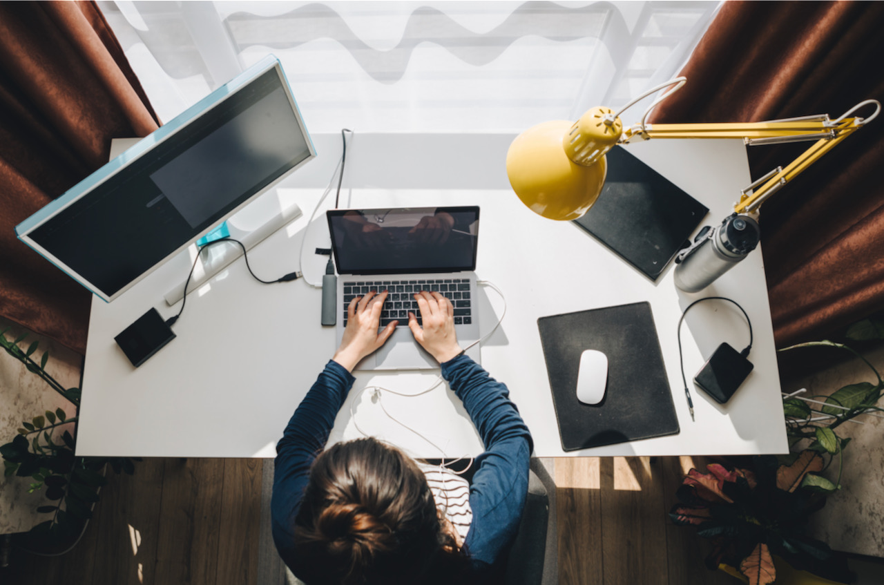Vue de dessus d'un poste de travail avec écran, ordinateur portable et lampe de bureau