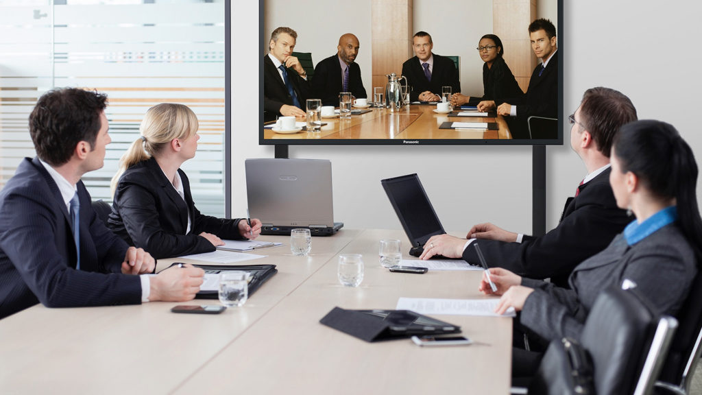 Salle de réunion équipée d'un écran de visioconférence où échangent des collaborateurs