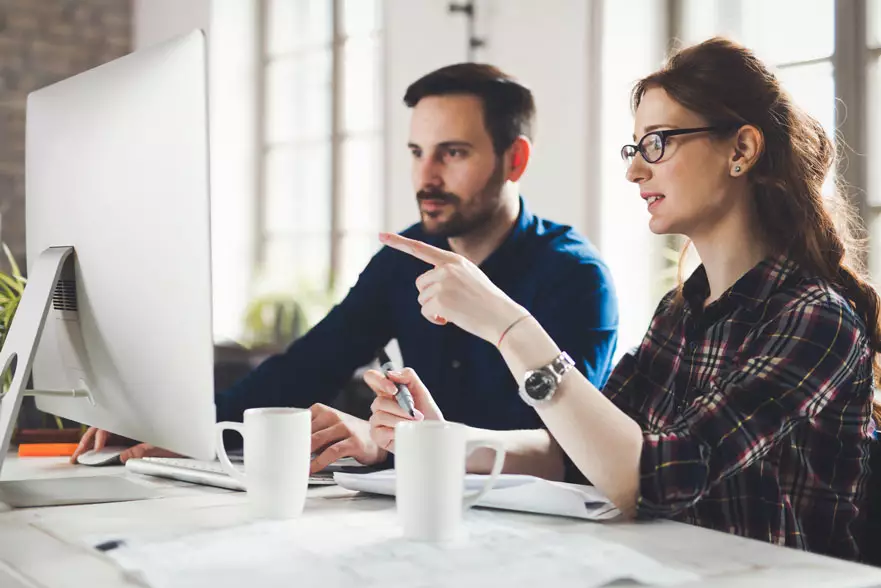 Deux collègues échangeant devant un iMac dans un bureau lumineux
