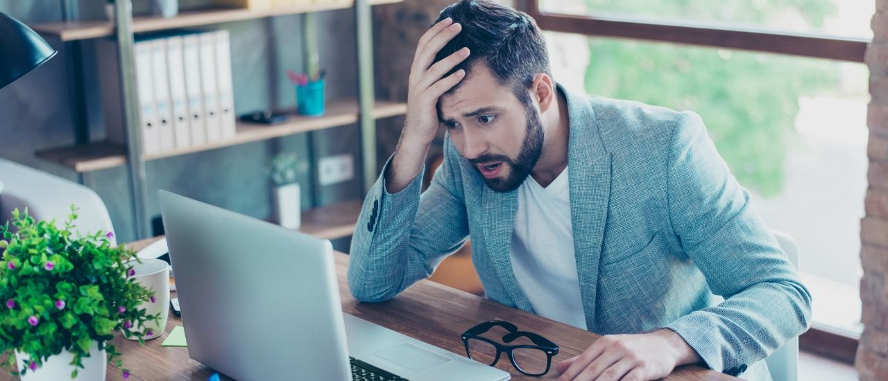 Homme inquiet, la main sur la tête, devant son ordinateur portable
