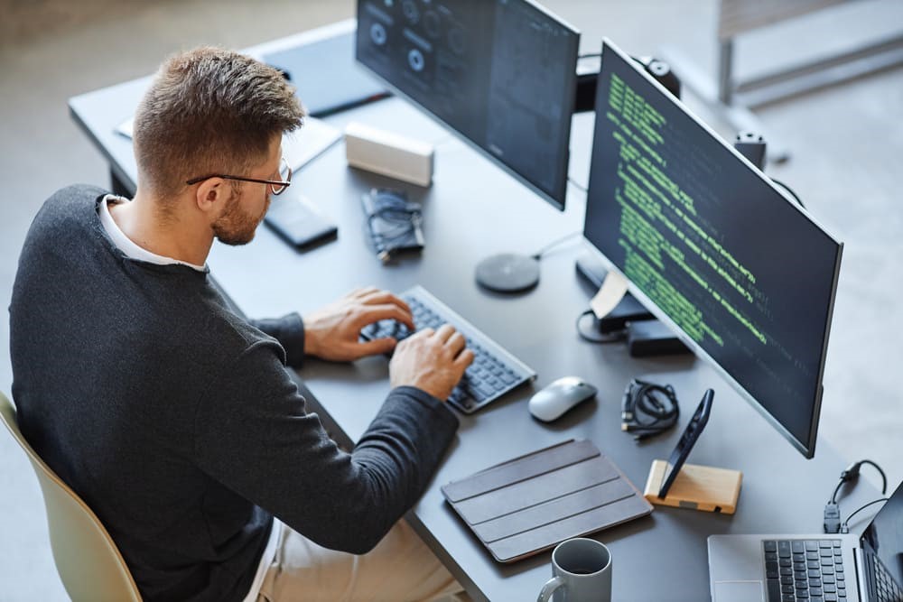 Développeur travaillant sur un poste équipé de deux écrans affichant du code