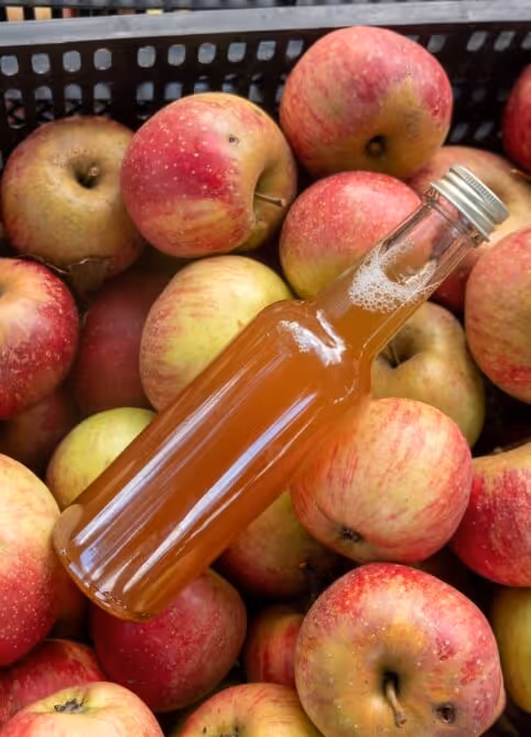 Bottle of amber liquid placed on a pile of red and yellow apples in a black container.