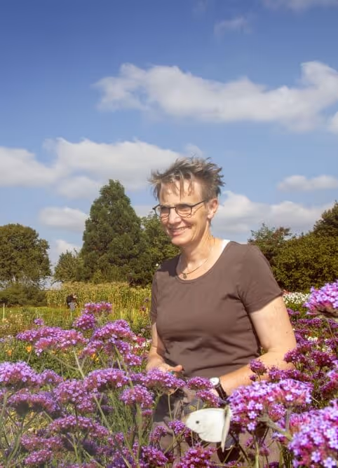 Smiling woman in glasses among purple flowers with a white butterfly on a sunny day.