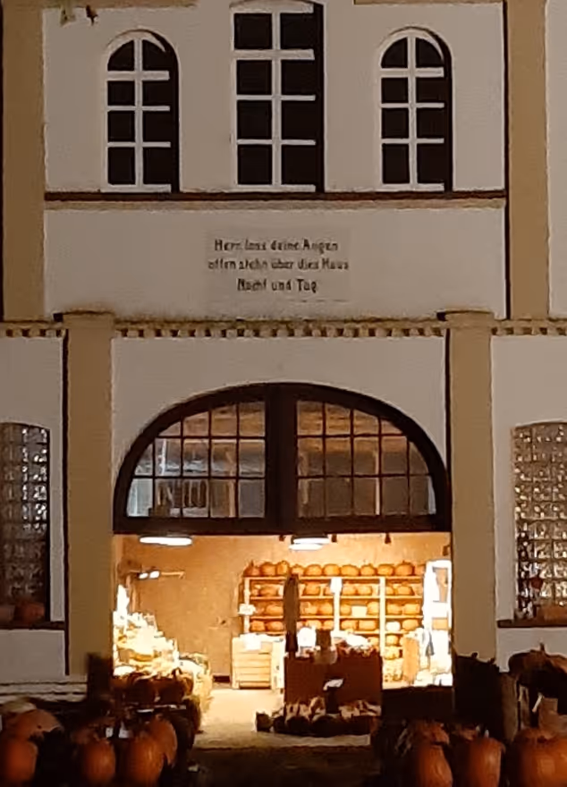 Store entrance at night with lit interior displaying shelves full of orange pumpkins and more pumpkins outside.