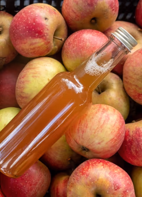 Glass bottle filled with amber liquid lying atop a pile of red and yellow apples.
