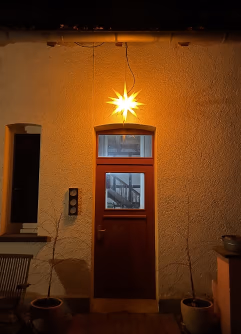 Glowing star-shaped light hanging above a wooden door on a beige stucco wall at night.