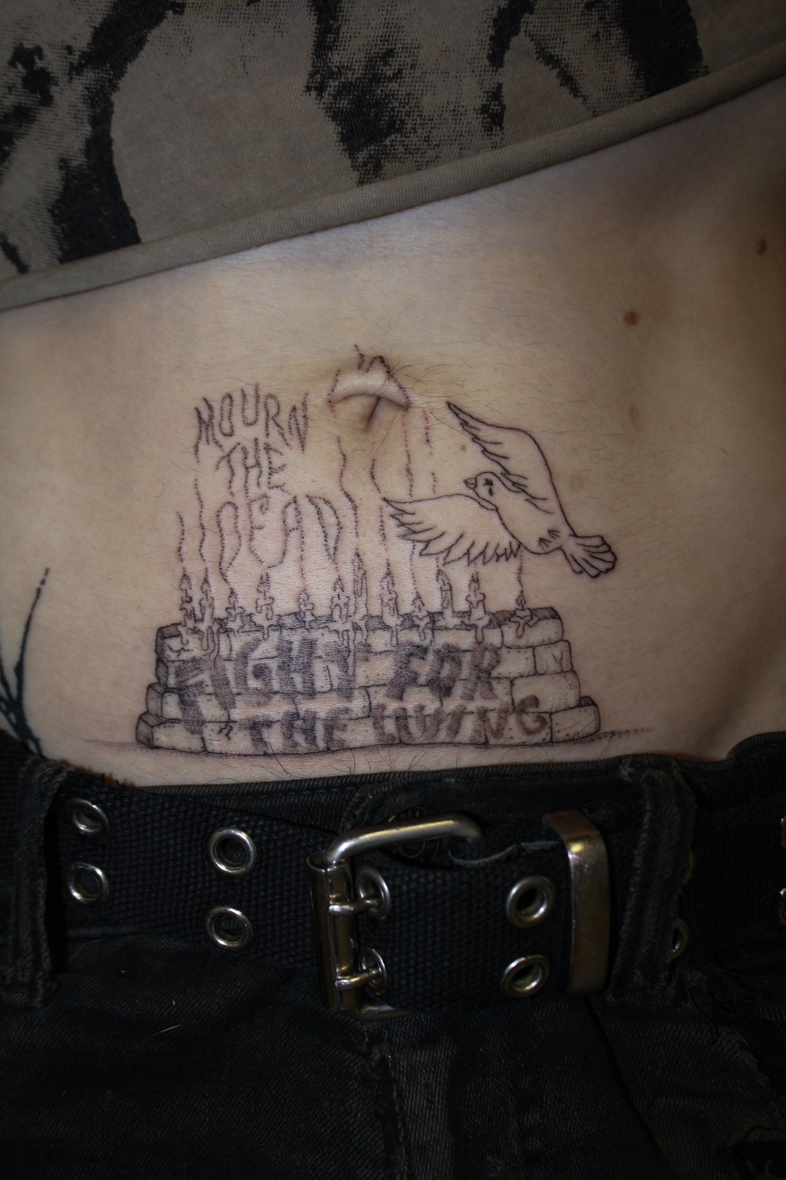 tummy tat of candles on a brick wall with a dove flying over, in the smoke it reads "mourn the dead" and in graffiti on the wall it reads "fight for the living)