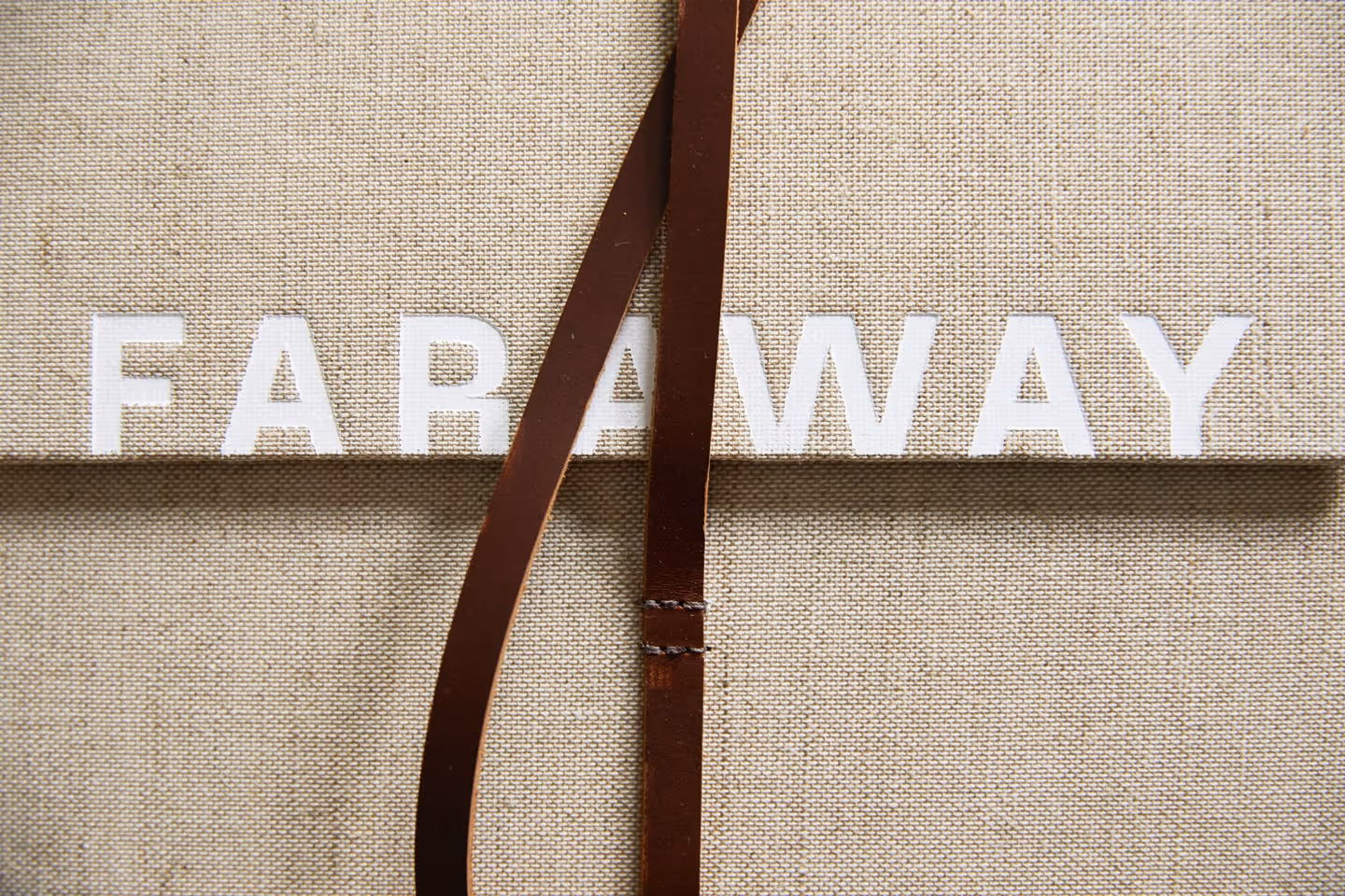 A beige textured surface with the word FARAWAY in white letters, partially covered by a brown leather strap.