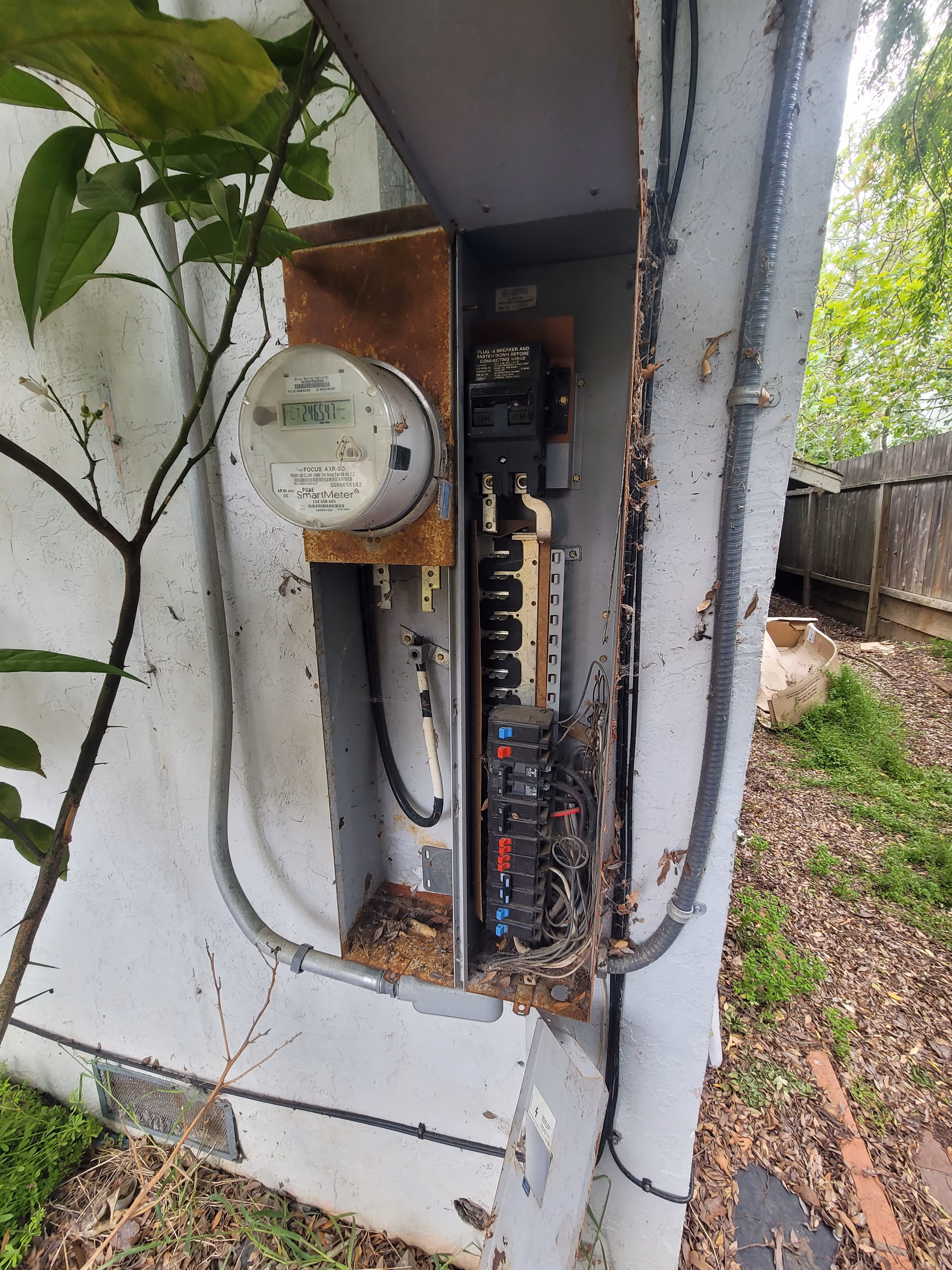 Exterior electric meter and open breaker panel mounted on the side of a house