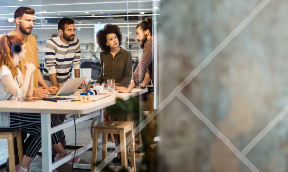 A team of people in a work environment standing around a table having a discussion - First Technology Cyber Security Solutions