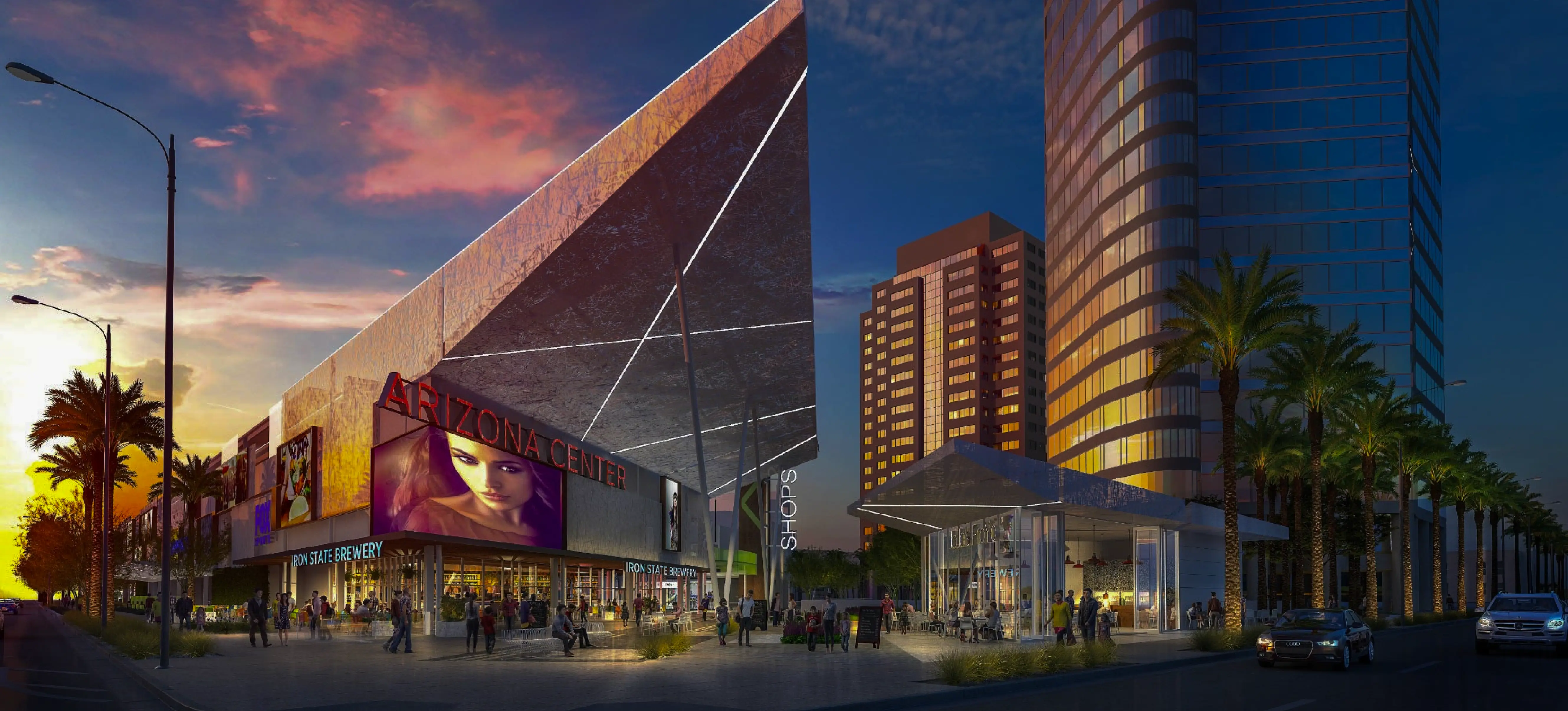 Evening view of Arizona Center with modern buildings, palm trees, shoppers, and cars on the street.