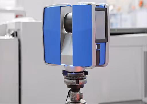 Blue and gray 3D scanner device mounted on a tripod in a modern indoor setting.