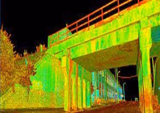 Underneath a concrete bridge at night with railing overhead and trees to the left.
