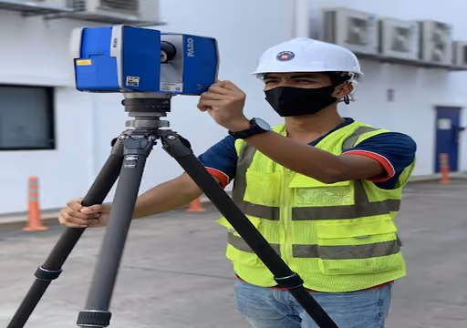 Engineer wearing a helmet and mask setting up a blue 3D scanner on a tripod outdoors.