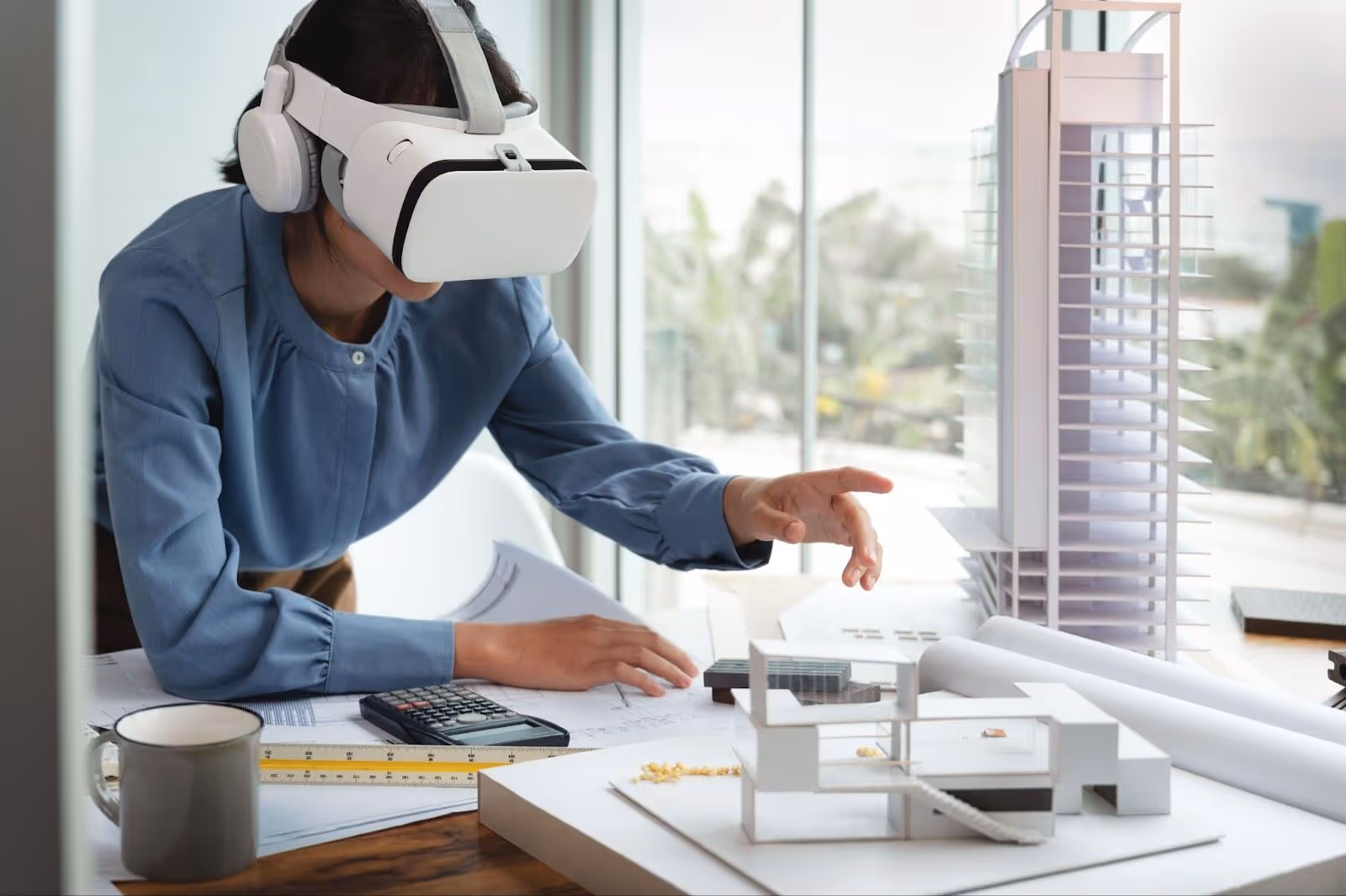 Person using a VR headset to interact with architectural models and blueprints on a table.