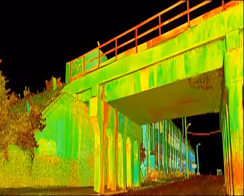 Infrared thermal image of a bridge and surrounding area at night showing heat variations in different colors.