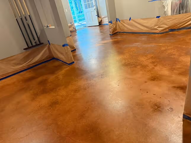 Room with freshly stained polished concrete flooring and walls protected by taped brown paper.