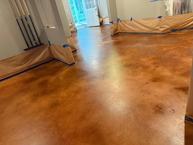 Room with freshly stained polished concrete flooring and walls protected by taped brown paper.