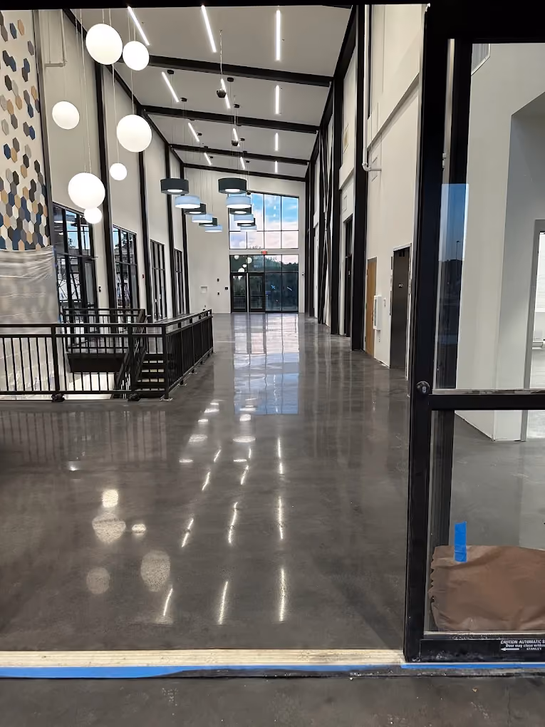 Modern interior hallway with polished concrete floor, high ceiling, pendant lights, and large windows.