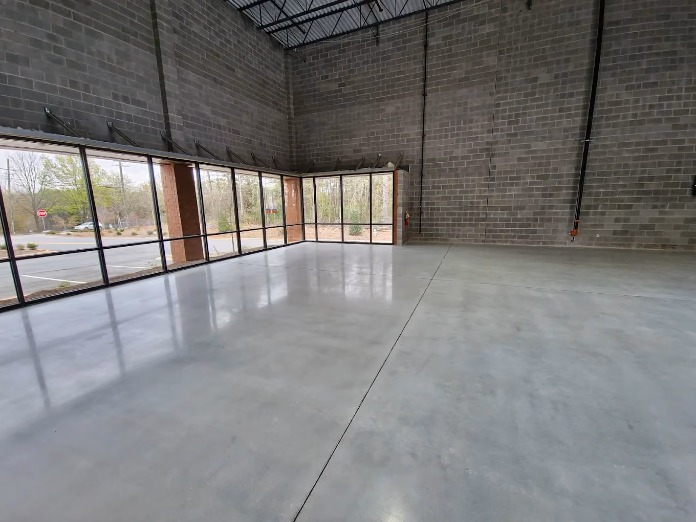 Empty warehouse interior with polished concrete floor and large windows showing outdoor trees.