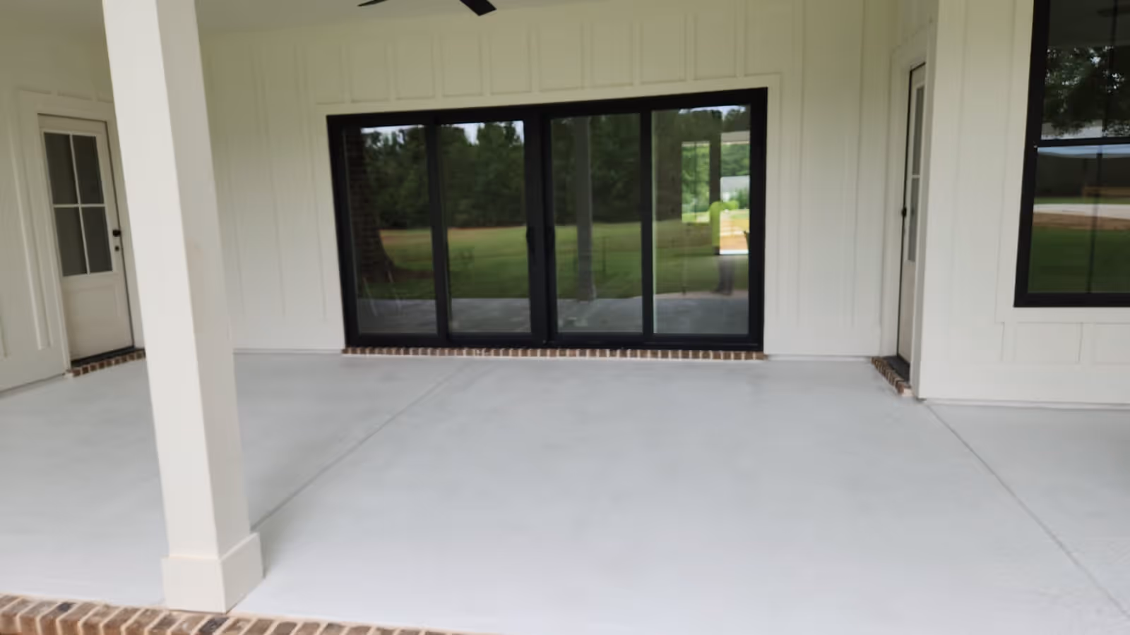 Covered patio with white resurfaced concrete floor, white walls, black framed sliding glass doors, and white door with window panels in atlanta, ga.