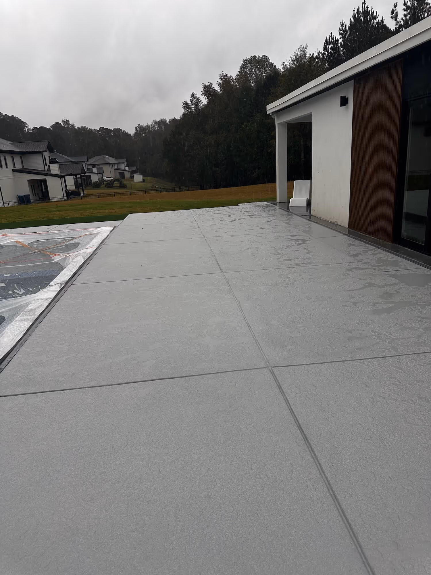 Wet concrete pool deck adjacent to a modern house with surrounding trees in atlanta.