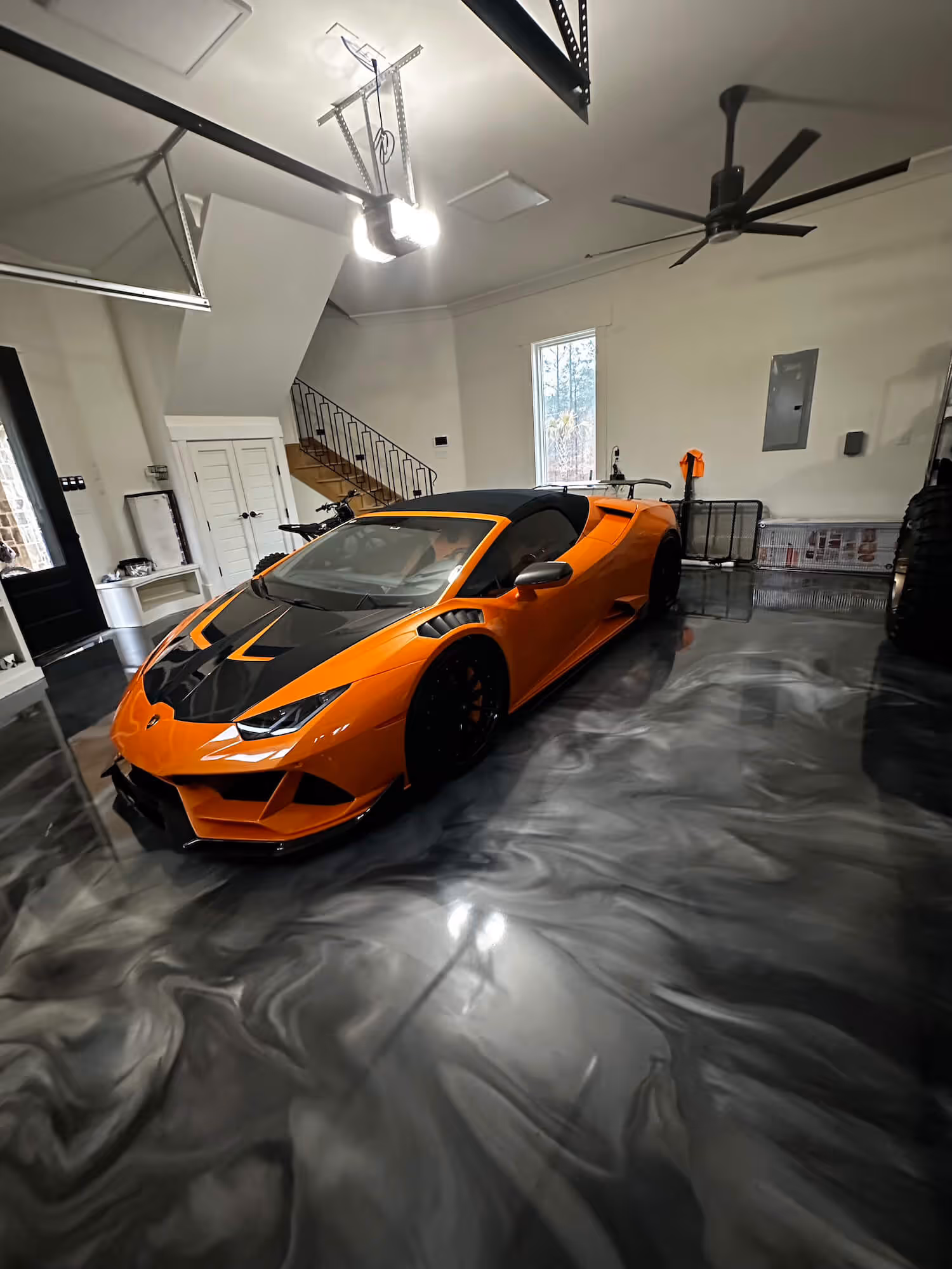 Orange and black sports car parked on a glossy metallic epoxy garage floor with a swirling gray and black pattern.